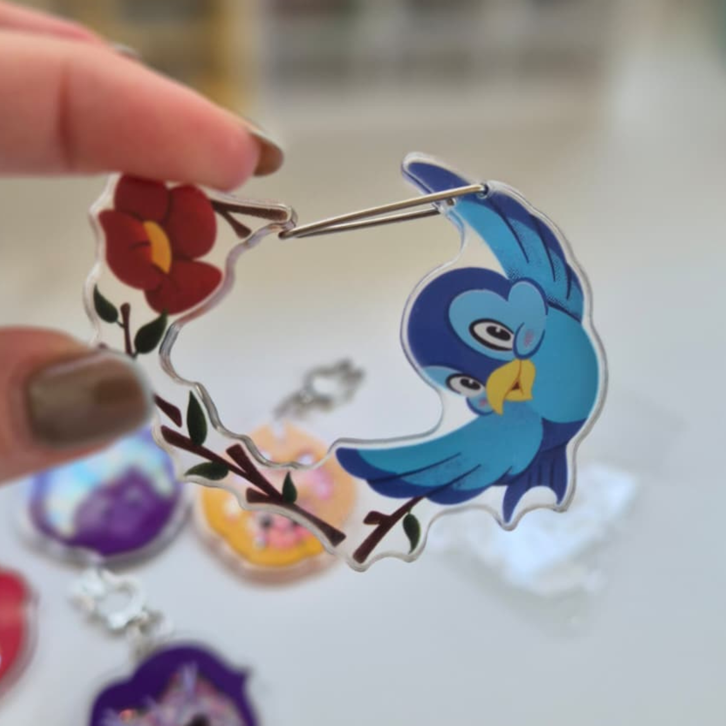 Blue bird and floral design pin held by a hand with a blurred background