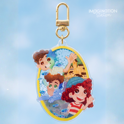 An oval acrylic keychain charm featuring cartoon characters from Finding Nemo, complete with a gold lobster clasp, set against a soft blue sky background. The 'IMAGINATION Station' logo is visible in the top right corner.