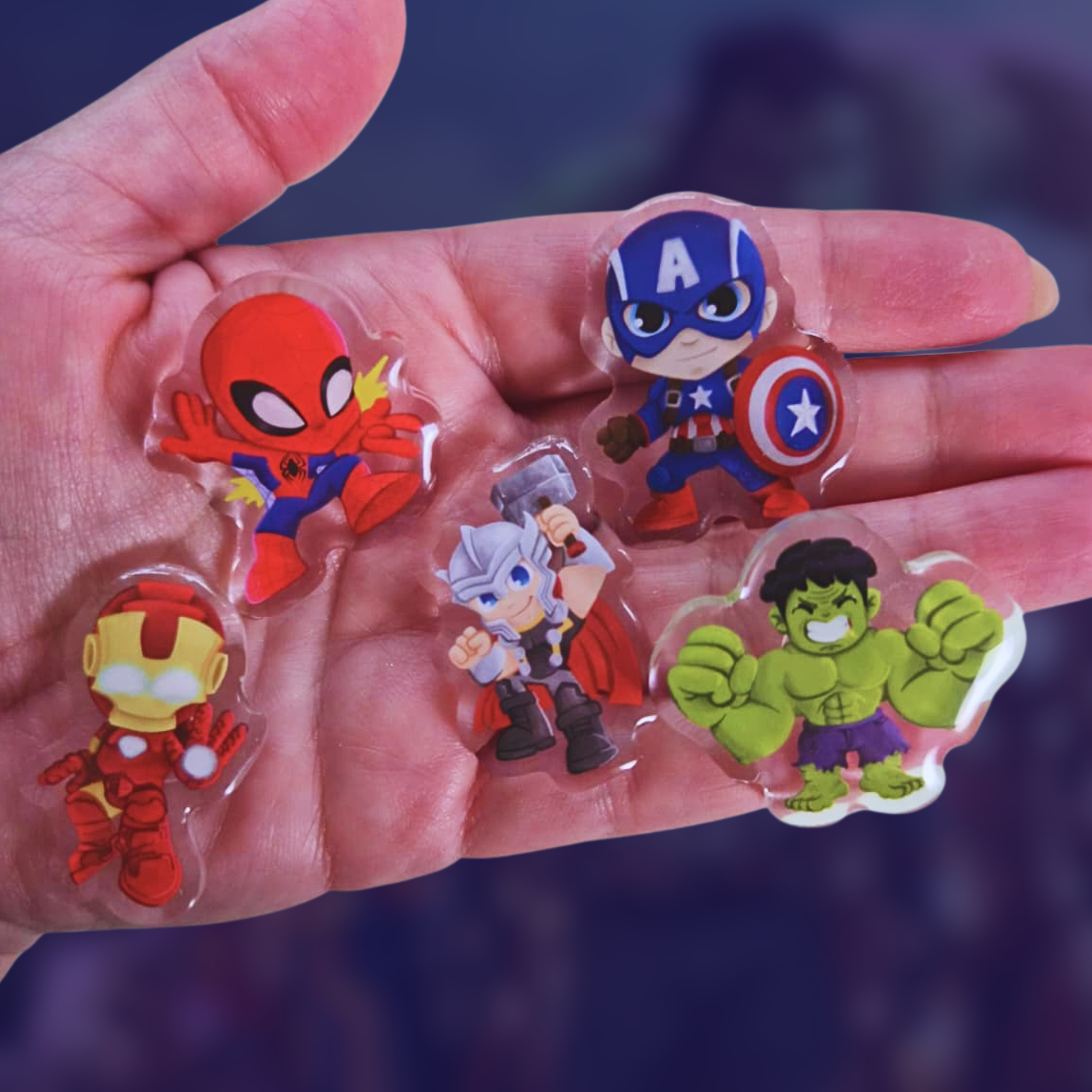 Hand holding superhero figurines including Spider-Man, Captain America, Iron Man, and Hulk against a dark background.