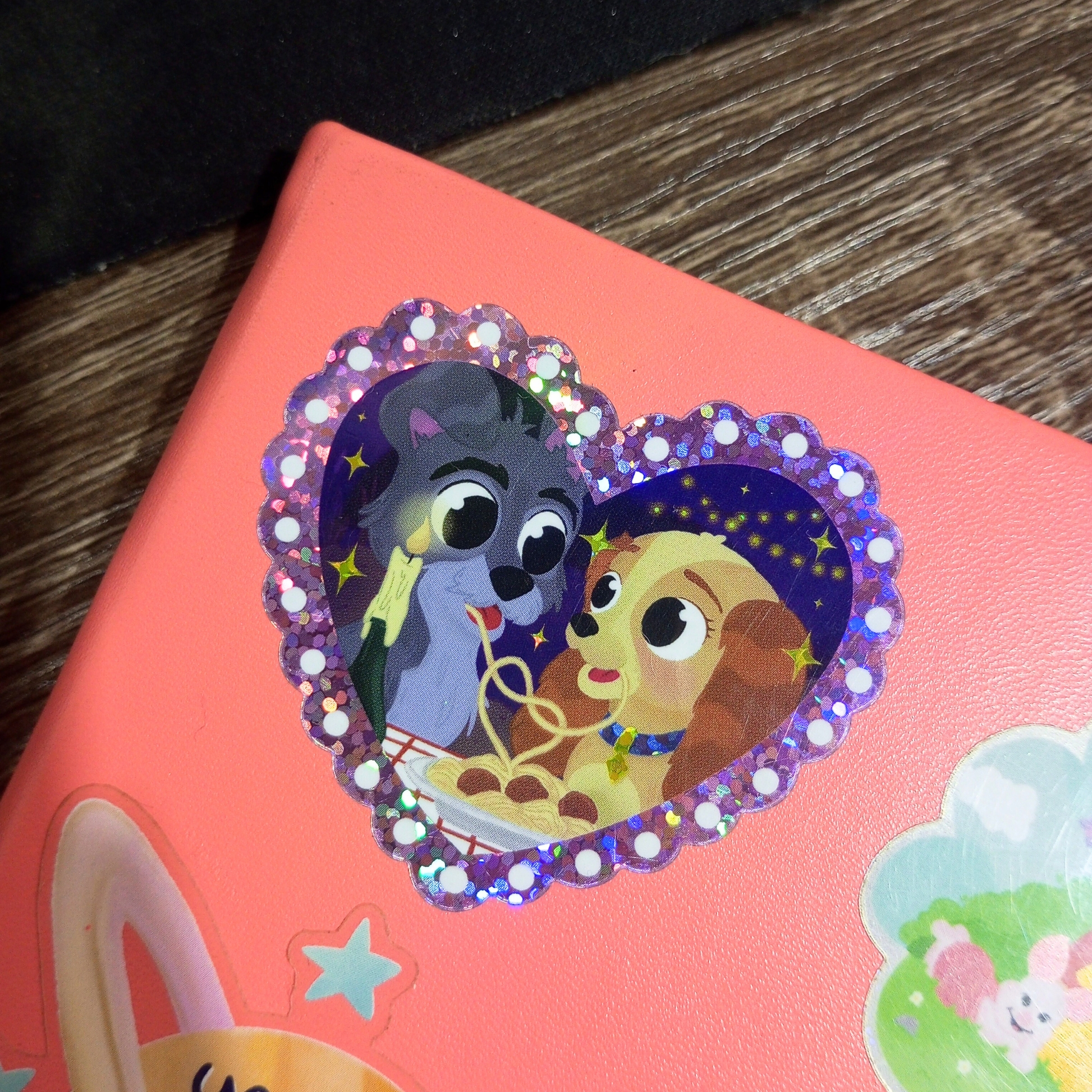 Pink notebook with a decorative sticker featuring cartoon characters on a wooden surface.