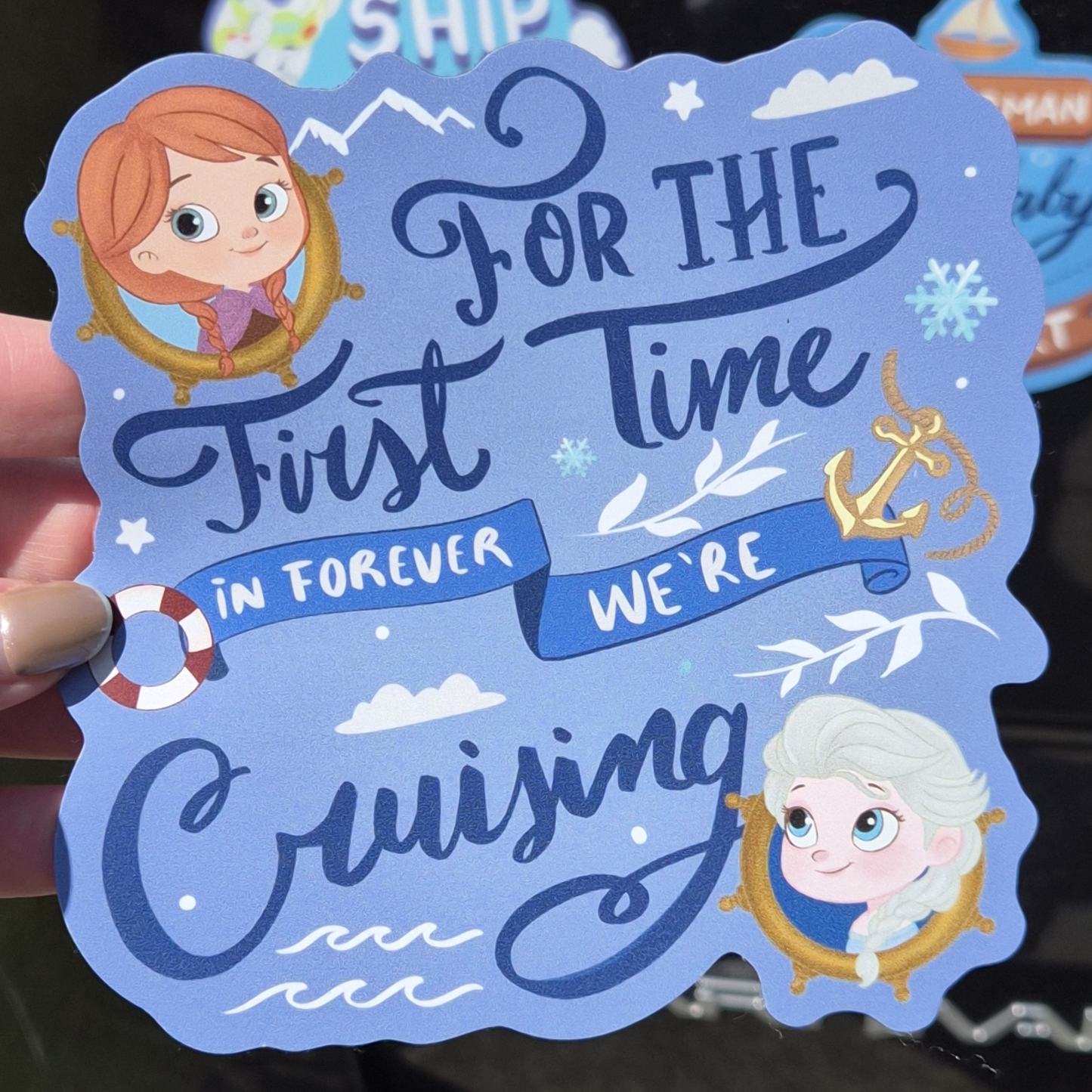 A hand holding a custom Frozen Disney cruise magnet. The blue design includes young Anna and Elsa, nautical details like an anchor and lifebelt, and the quote: "FOR THE first Time IN FOREVER WE'RE Cruising".
