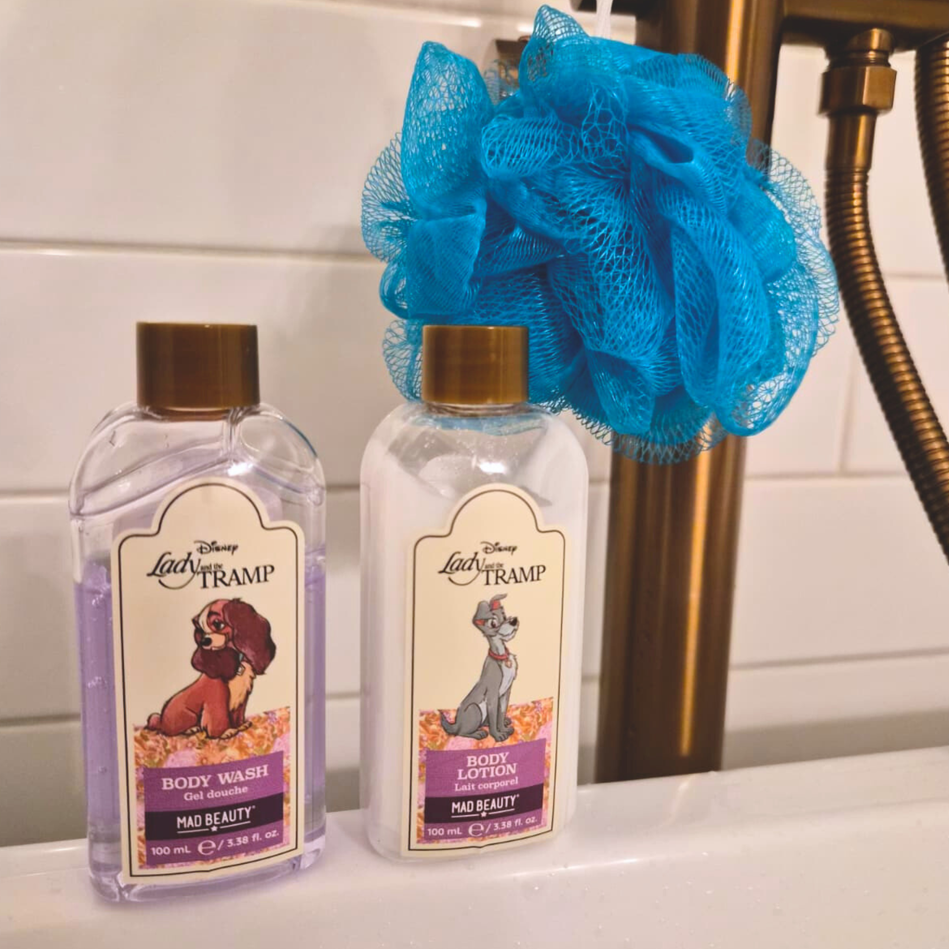 Two bottles of Disney Lady and the Tramp body wash and lotion with a blue loofah on a bathroom counter.