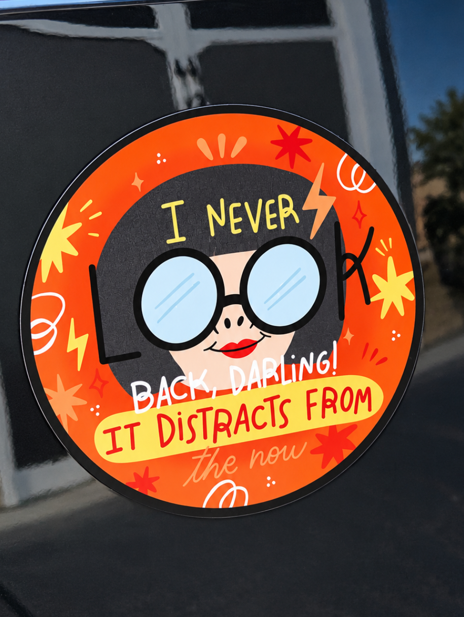 A round car window sticker with a cartoon illustration of a woman wearing oversized glasses and the text 'I NEVER BACK-DARLING! IT DISTRACTS FROM the new', shown applied to a black car door.