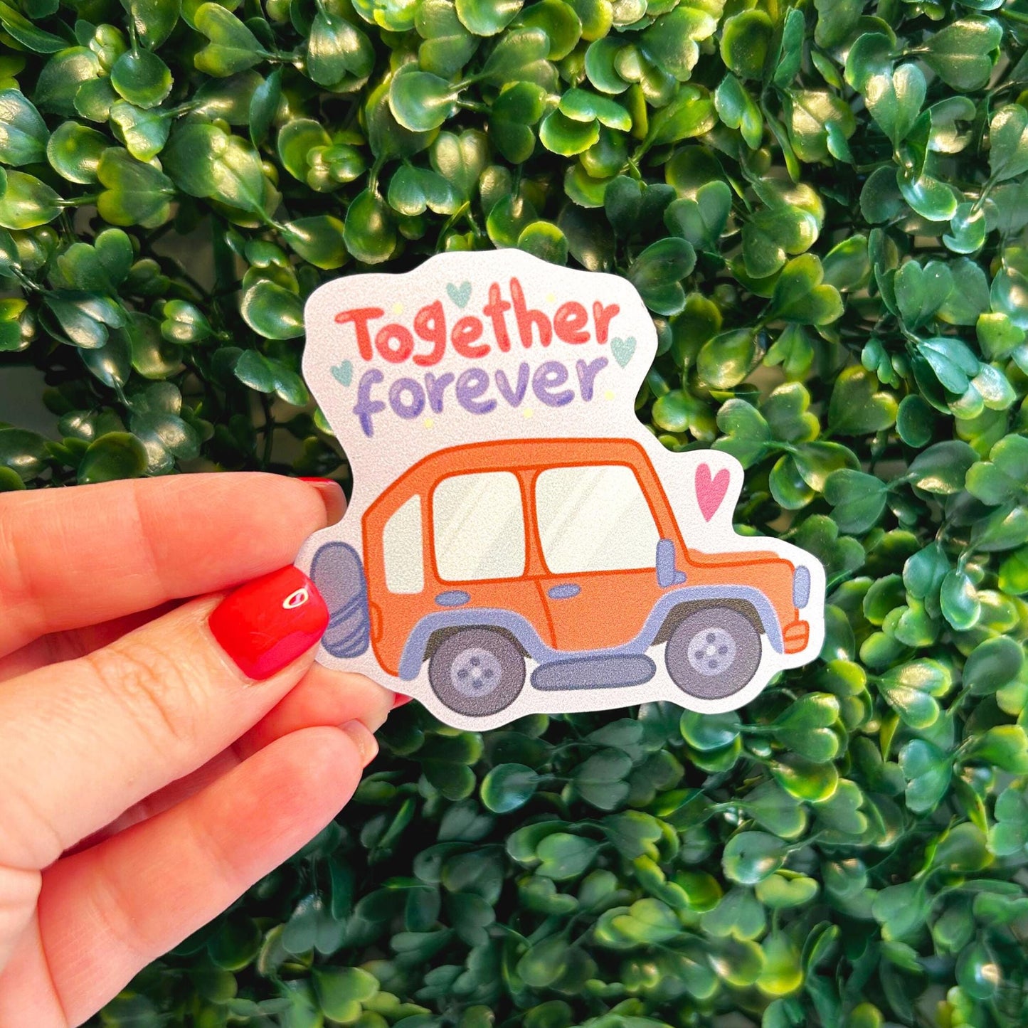 car magnet with 'Together forever' text and a car design held in front of green foliage