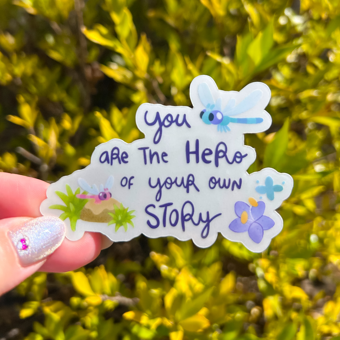 Sticker with motivational quote held by a hand against a green leafy background