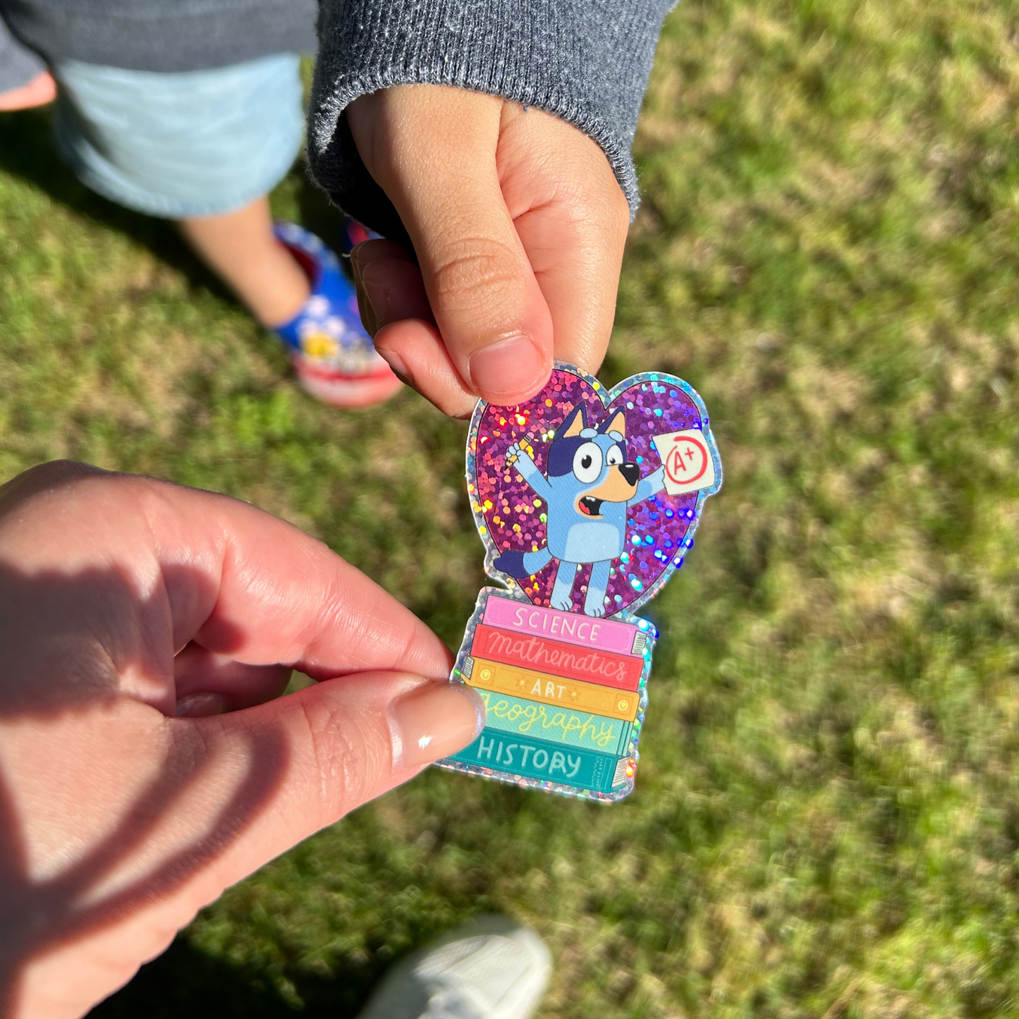 Colorful sticker held by two hands against a grassy background