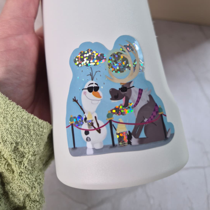 White mug with cartoon characters Olaf and Sven on a blue background, held by a person.