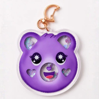 A purple bear-shaped keychain charm with a gold metal clasp, featuring cute cartoon eyes, heart-shaped cutouts, and colorful glittery inner details, shown on a plain white background.