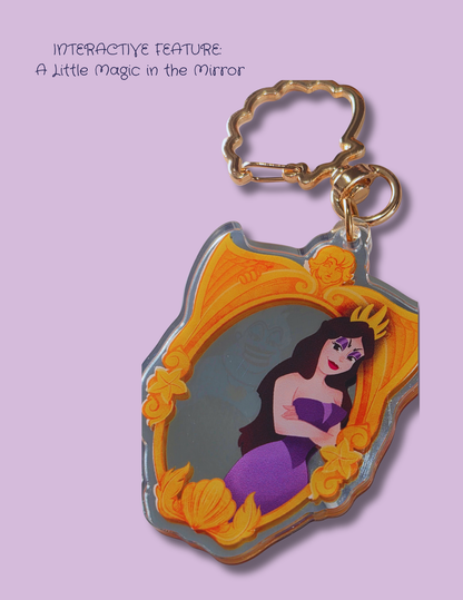 An acrylic keychain featuring an illustration of a mermaid inside an ornate golden mirror frame, shown on a light purple background with text that reads 'INTERACTIVE FEATURE: A Little Magic in the Mirror.'.