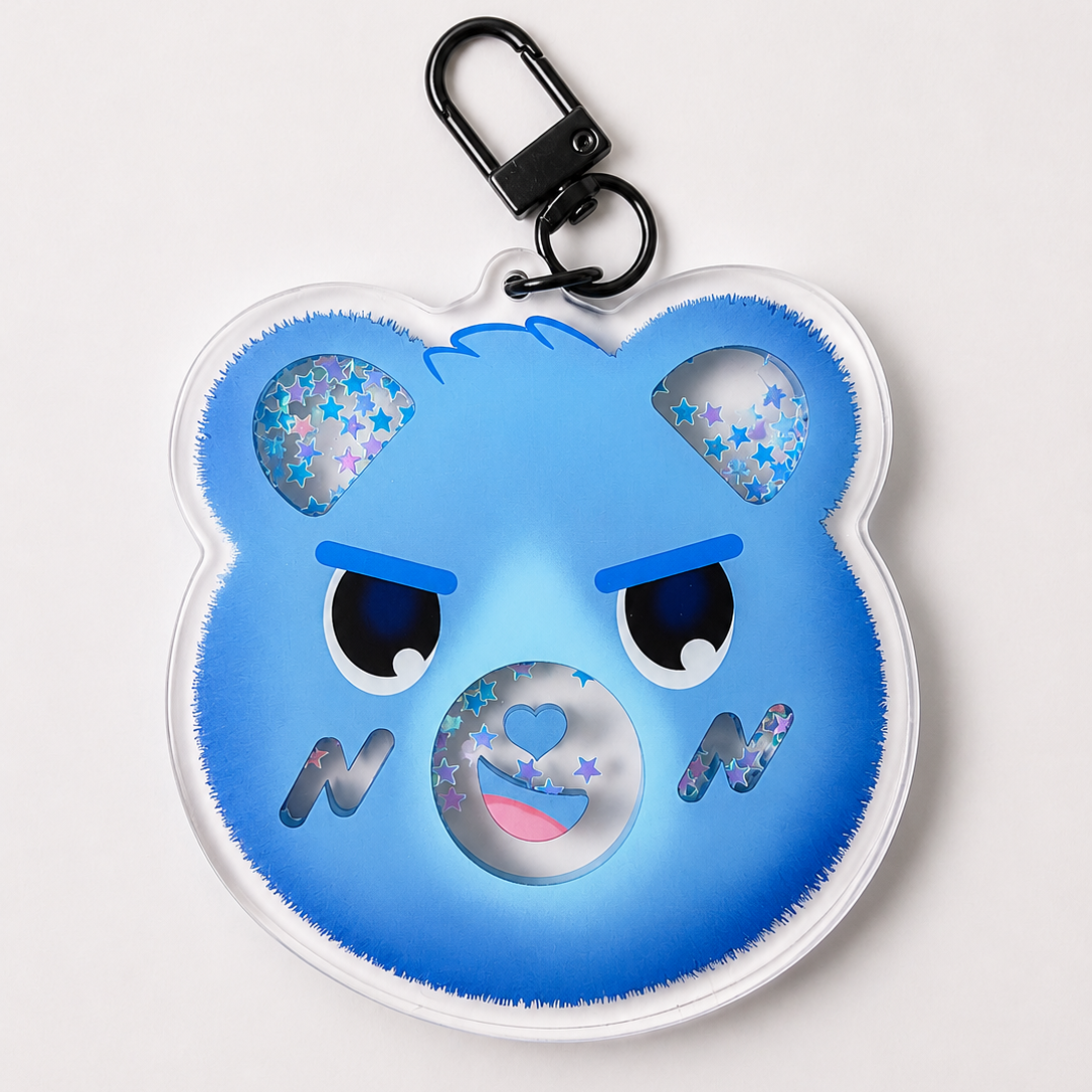 A blue bear-shaped keychain with a black carabiner clip, featuring glittery star details in the ears and a glittery circular mouth on a light gray background.