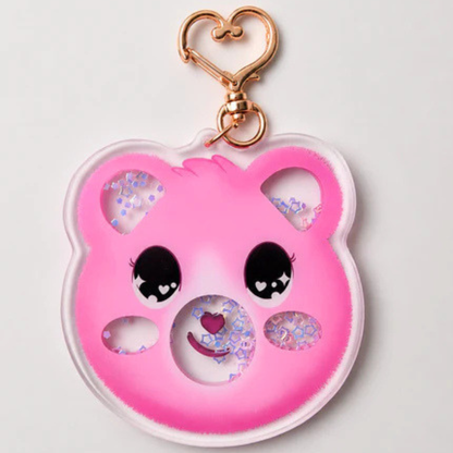 A pink bear-shaped keychain with a gold heart-shaped clasp, featuring cute cartoon eyes and a smiling face with glitter-filled shaker holes.