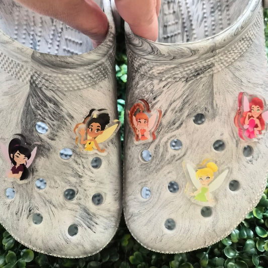 Pair of gray clogs with fairy character stickers on a green grass background