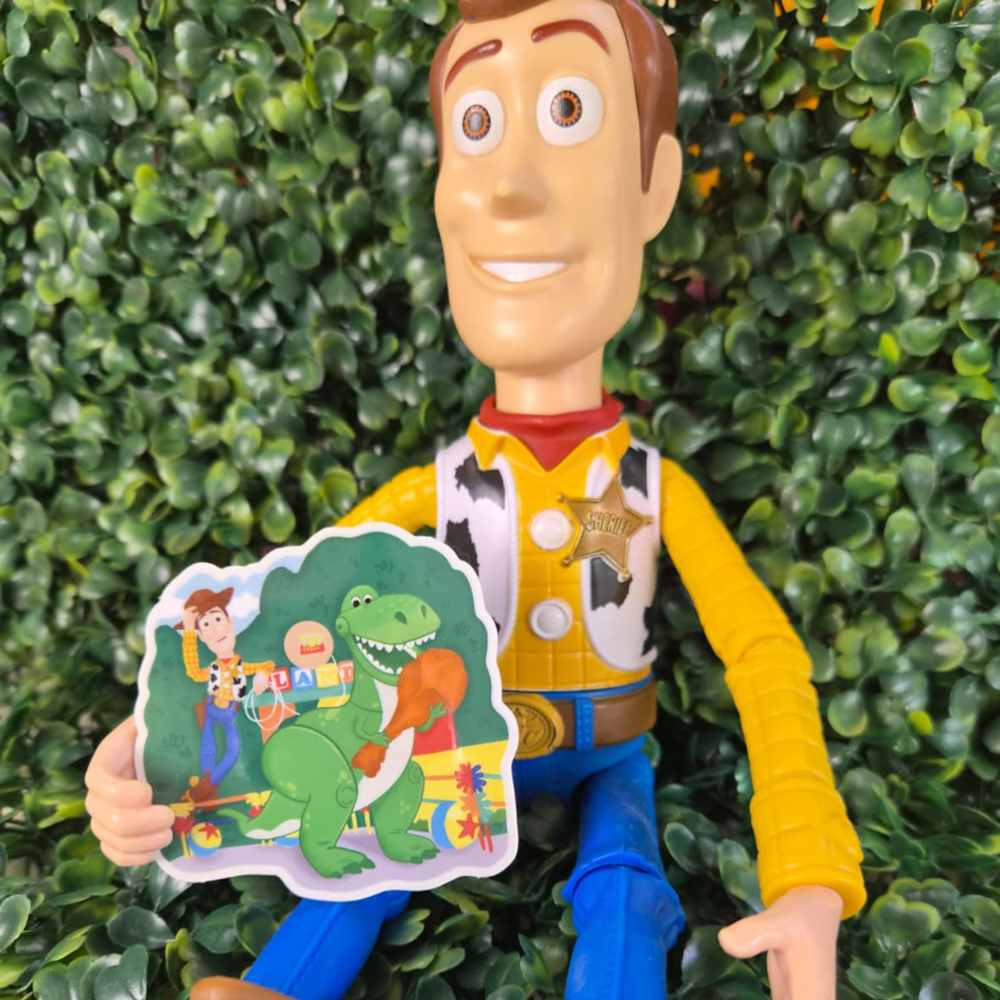 Toy Story figure holding a dinosaur-themed card against a green bush background